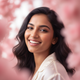Close-up portrait of a smiling young South Asian woman, mid-20s, with warm eyes, against a soft, blurred background.